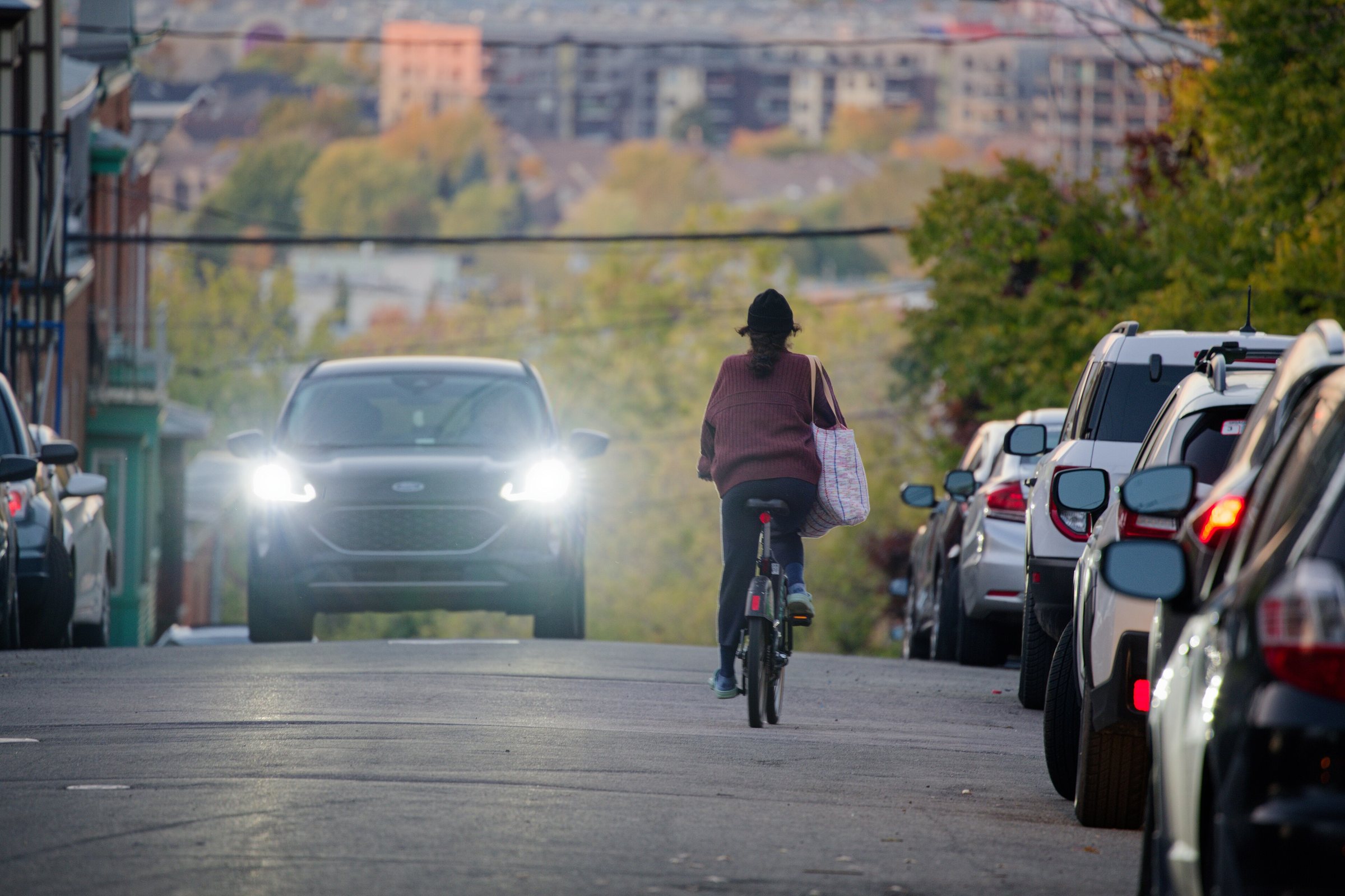 A cyclist in a dark red top and hat rides away down a Quebec City street lined with parked cars.